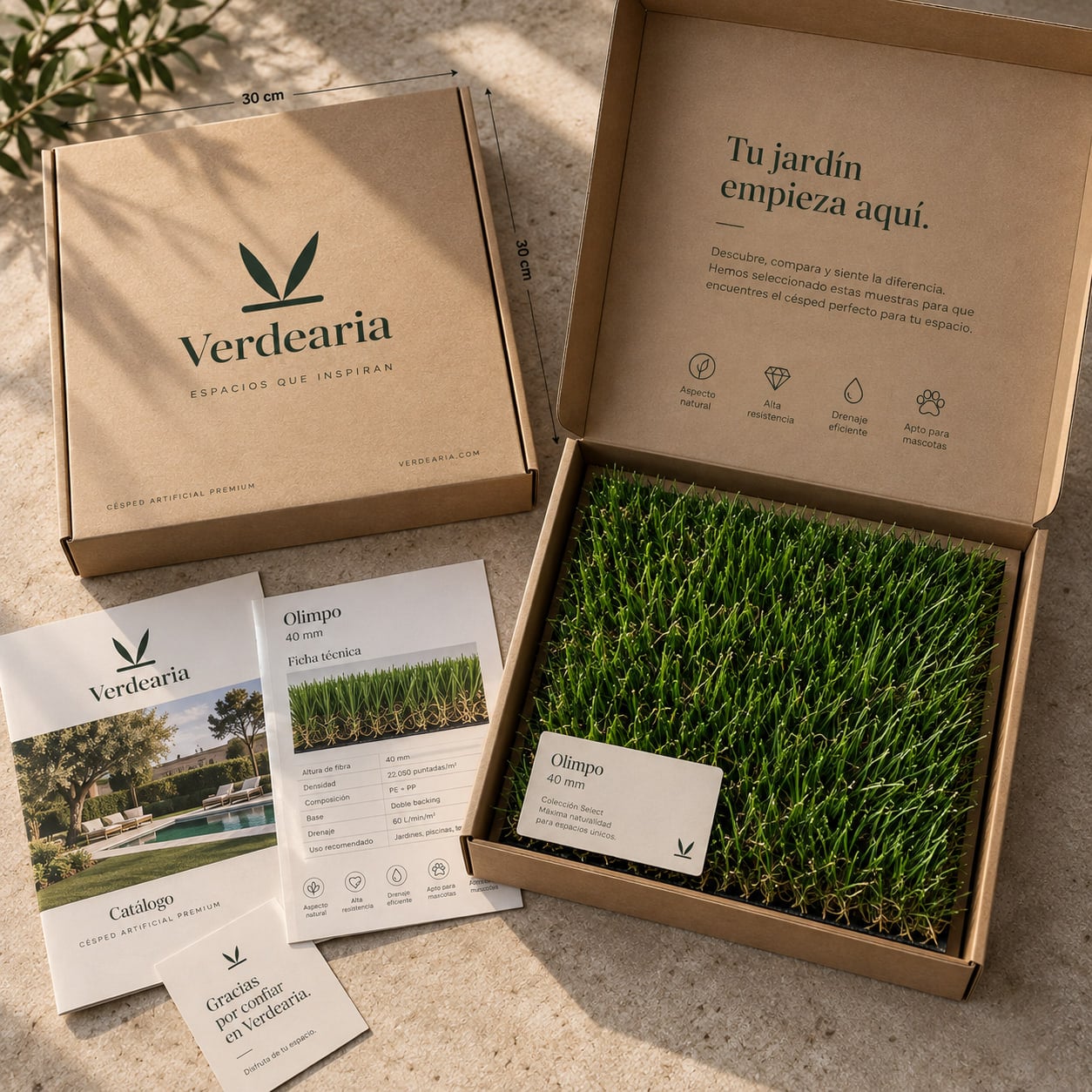 Caja de cartón abierta con la marca Verdearia, con una muestra de césped artificial encajada dentro junto a su ficha técnica, un catálogo impreso y una tarjeta de agradecimiento
